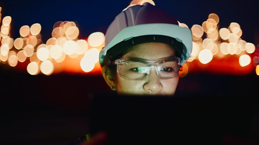 Female Engineer Using Digital Tablet For Work At Electrical Power Plant At Night Time.